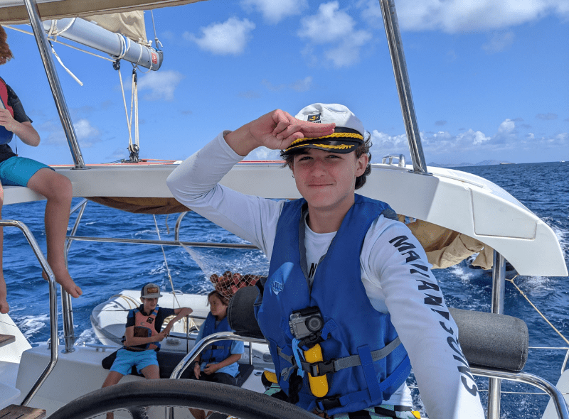 high school boy at helm of yacht sailing through the Caribbean on liveaboard summer program