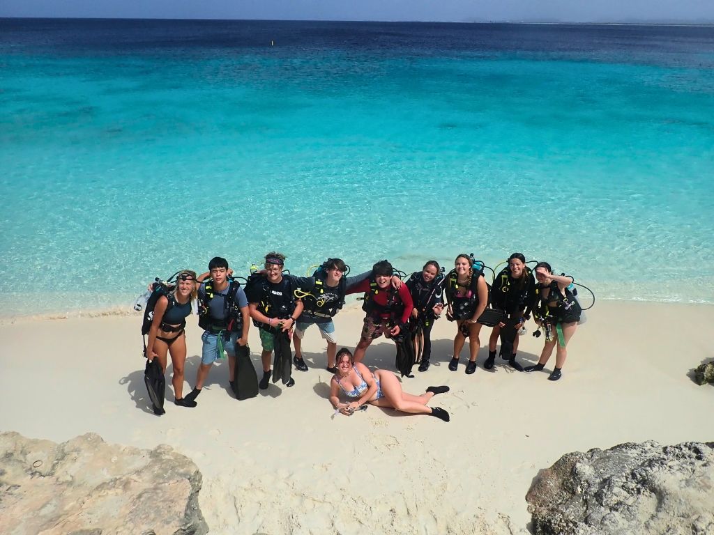 Broadreach students in dive gear pose on white sand beach in Bonaire with turquoise waters